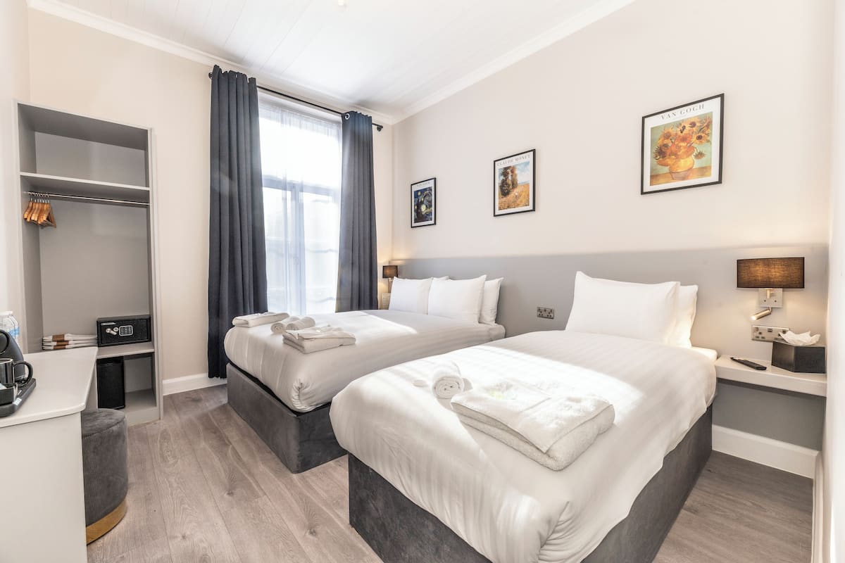 A hotel room with two beds, a desk, a wardrobe, and a window with curtains.
