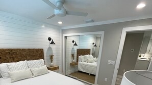 Un dormitorio moderno con una cama grande, un ventilador de techo, un espejo y una mesita de noche con lámpara.