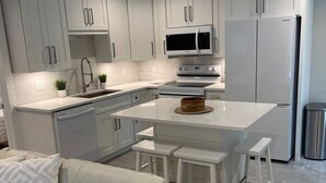 Una cocina moderna con armarios blancos, una isla central con taburetes, microondas integrado y un refrigerador de acero inoxidable.