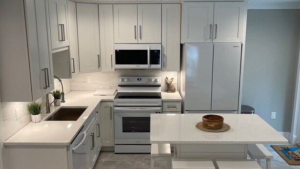 Una cocina moderna con armarios blancos, microondas integrado, refrigerador Samsung y un comedor con banco.