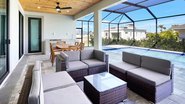 Un patio moderno al aire libre con mobiliario de mimbre, una piscina cubierta por vidrio y vistas a casas vecinas.
