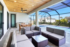 Un patio moderno al aire libre con mobiliario de mimbre, una piscina cubierta por vidrio y vistas a casas vecinas.
