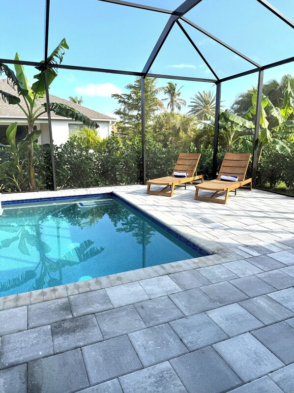 Zona de piscina con dos sillas reclinables de madera y una estructura de vidrio.