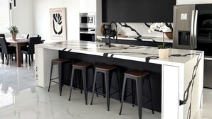 Una cocina moderna con una isla central, taburetes de bar, una cafetera y un refrigerador.