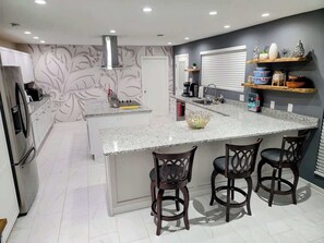 A modern kitchen with a large island, bar stools, a built-in oven, and a decorative backsplash. - Downtown Savannah Oasis w Heated Pool & Spa (Savannah)