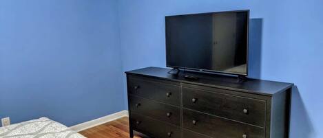 Un dormitori amb un taulell de fusta fosca, un televisor de pantalla plana a sobre i un edredó estampat.