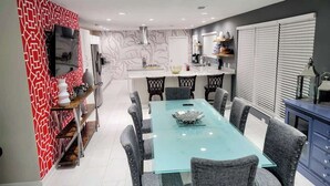 A modern kitchen with a glass dining table and chairs, a built-in oven, and a TV mounted on the wall. - Downtown Savannah Oasis w Heated Pool & Spa (Savannah)