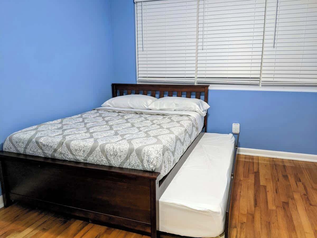 Een eenpersoonsbed met een bedsprei met dessin, een houten hoofdbord en een witte matras aan het voeteneind.