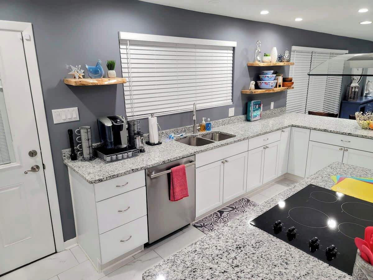 Una cocina moderna con armarios blancos, encimera de granito, horno empotrado y ventana con persianas.