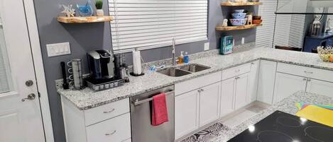 Una cocina moderna con armarios blancos, encimera de granito, horno empotrado y ventana con persianas.