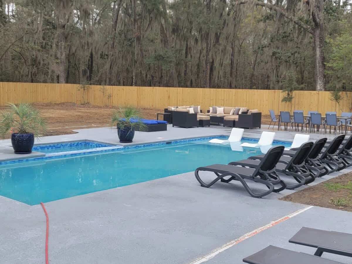 Une piscine rectangulaire bordée de carreaux bleus, entourée de chaises longues et d’une clôture en bois.