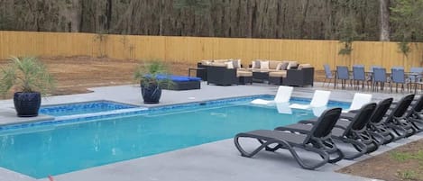 Une piscine rectangulaire bordée de carreaux bleus, entourée de chaises longues et d’une clôture en bois.