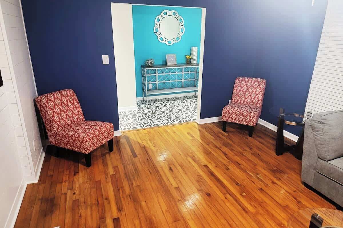 Une pièce avec deux fauteuils à motifs, un mur d’accent bleu, un plancher en bois et une petite table avec un miroir.