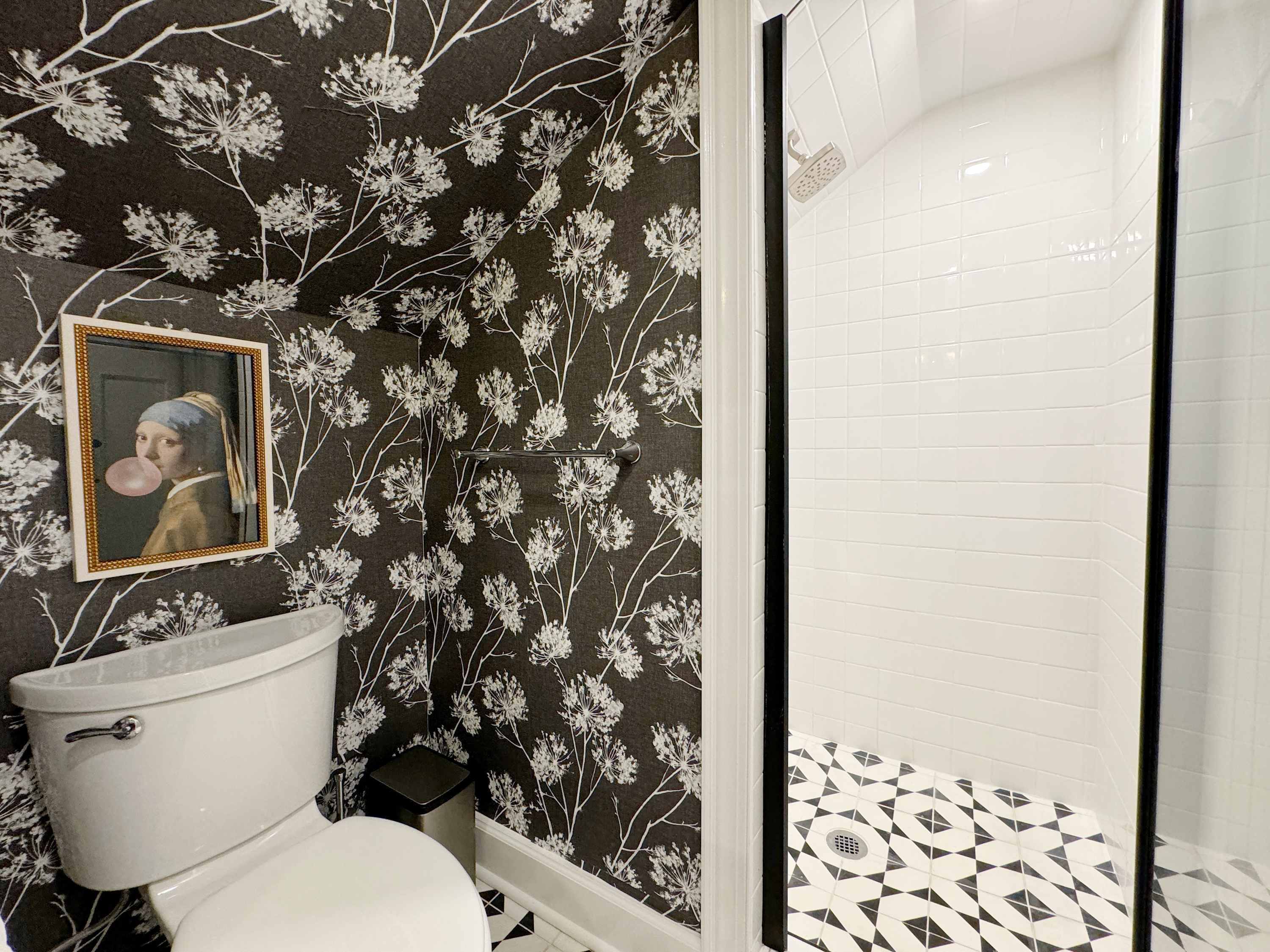 A bathroom with a toilet, a shower with a geometric tile floor, and a wall with a floral pattern.