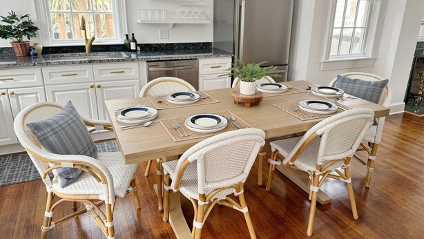 A dining area with a wooden table set for four, surrounded by wicker chairs, a stainless steel refrigerator, and a potted plant. - Spacious 3-Floor Downtown Retreat - Prime Location (Savannah)