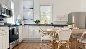 A modern kitchen with white cabinetry, stainless steel appliances, and a dining area with wicker chairs. - Spacious 3-Floor Downtown Retreat - Prime Location (Savannah)