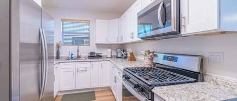 A modern kitchen with white cabinets, a stainless steel refrigerator, a built-in microwave, and a gas stove.