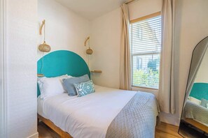 A bedroom with a bed, a window with curtains, and a mirror.