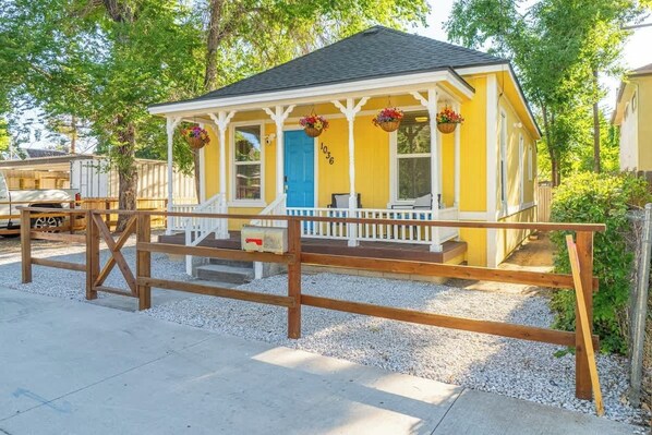 A yellow building with a blue door, white porch, and wooden fence.