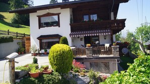 Un chalet à deux étages doté d’un balcon en bois, d’un petit jardin et d’un espace barbecue en pierre.