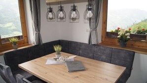 Un coin repas avec une table en bois, des bancs recouverts d’un tissu gris, une plante en pot et un ordinateur portable posé sur la table.