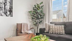 A living room with a wooden coffee table, a grey sofa with patterned cushions, a potted plant, and a framed artwork on the wall. - Spacious 6BR - Sleeps 22 - Hot Tub & Pool Access (Meridian)