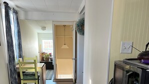 Un pasillo con suelo de madera, un comedor con mesa y sillas, y un microondas sobre un mueble de madera.