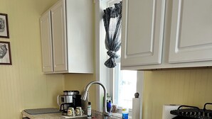 Una cocina con armarios blancos, encimera de granito, cafetera, tostadora y ventana con cortinas estampadas.