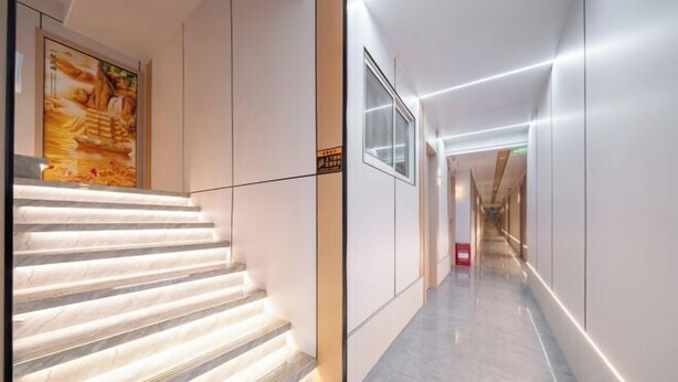 Un pasillo moderno de hotel con una escalera de mármol, una obra de arte enmarcada y un interior limpio y bien iluminado.