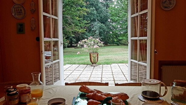 Porta aperta su un giardino con un tavolo apparecchiato per la colazione, con croissant, caffè e succo di frutta.