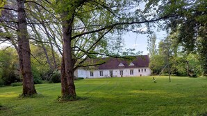 Un grande edificio bianco con una facciata simmetrica, circondato da un prato curato e alberi maturi.