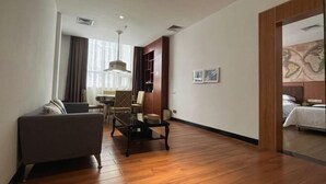 A spacious living area with a sofa, a coffee table, and a dining table with chairs. There is a wooden floor and a large window with curtains. - Xindi Hotel (Guangzhou Cultural Tourism City Huaguoshan Subway Station) (Guangzhou)