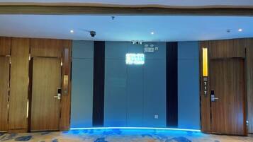 Una camera d'albergo con una porta di legno massiccio, un tappeto blu con motivo floreale e un lampadario moderno sopra la porta.