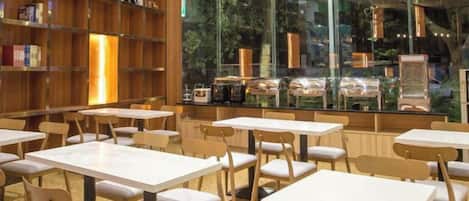 A café with tables and chairs, a bookshelf, and a view through large windows.