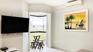 Una sala moderna con un televisor de pantalla plana, un sofá, una mesita con sillas y un cuadro que representa una escena de atardecer.