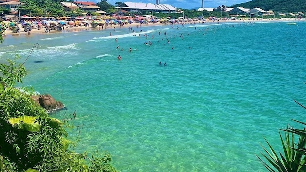 Una playa con agua turquesa cristalina, gente nadando y una hilera de sombrillas.