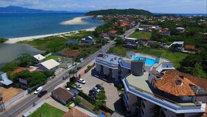 Vista aérea de un pueblo costero con un edificio destacado que tiene piscina, rodeado de casas residenciales y una playa.