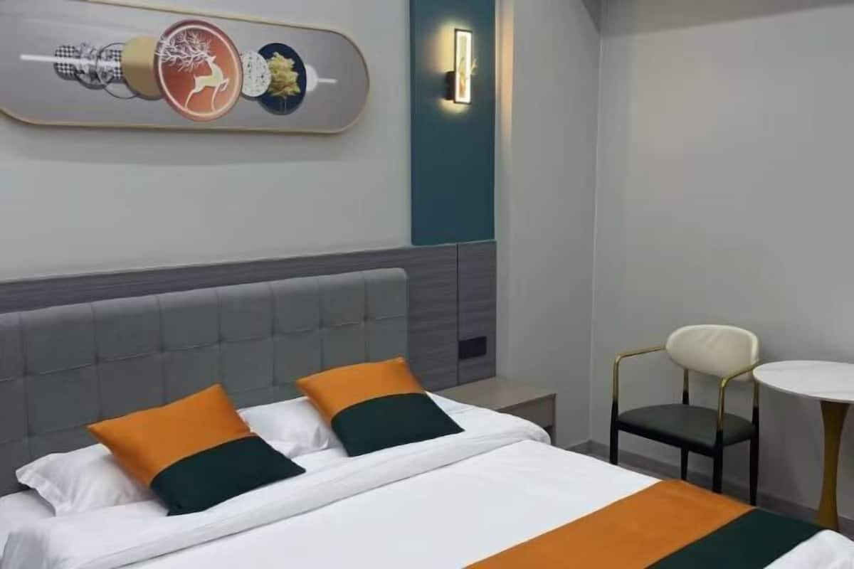 Une chambre d’hôtel comprenant un lit, deux oreillers, une table de chevet, une chaise, une table et un luminaire fixé au mur.