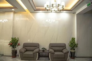 Un hall con dos sillones de cuero, una mesita, una araña y plantas en macetas.