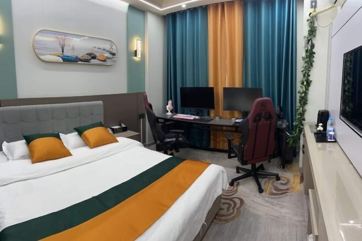 Une chambre d’hôtel avec un lit, un bureau, deux chaises, une télévision et une fenêtre avec des rideaux.