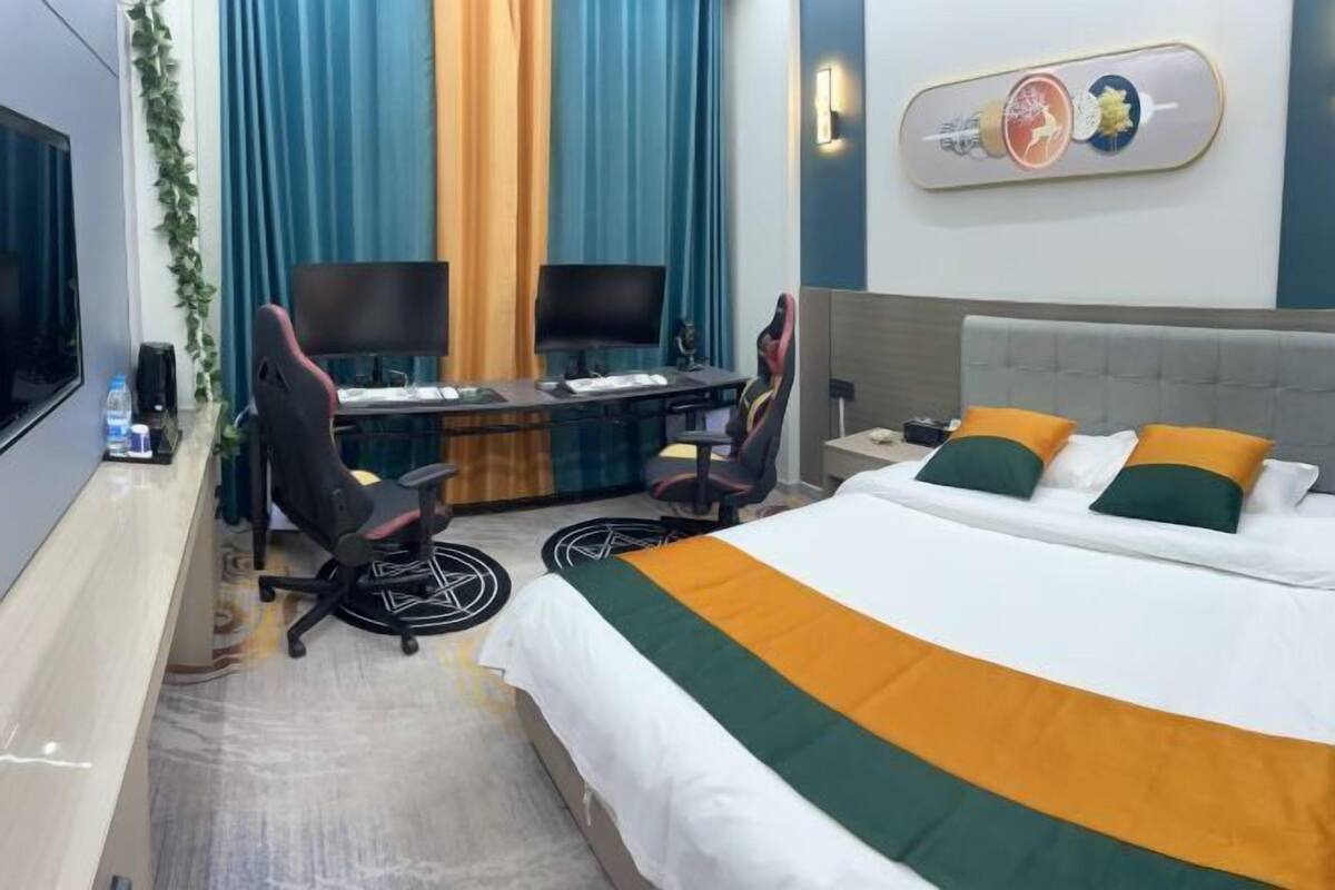 Une chambre d’hôtel équipée d’un lit, de deux bureaux avec des ordinateurs, d’une télévision et d’une œuvre d’art accrochée au mur.
