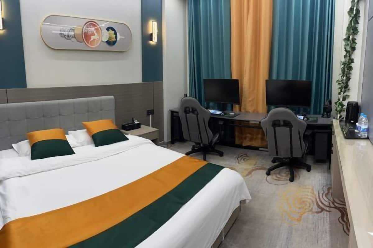 Une chambre d’hôtel comprenant un lit, deux bureaux avec des ordinateurs, une télévision et un élément décoratif fixé au mur.