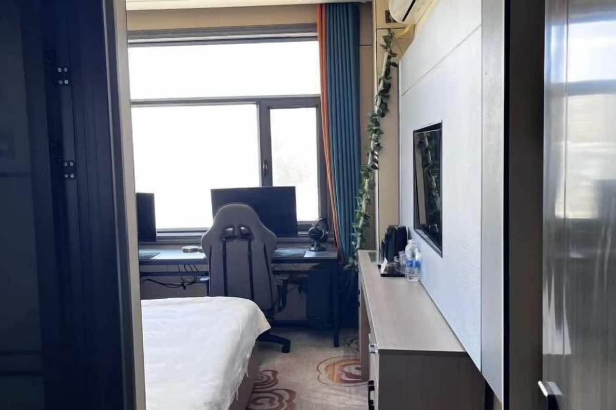 Une chambre d’hôtel avec un lit, un bureau avec un ordinateur, une chaise et une fenêtre avec des rideaux.