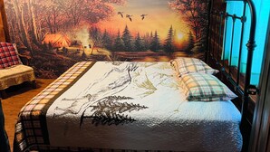 A bedroom with a large forest-themed tapestry on the wall, a bed with a checkered bedspread, and a window with a curtain.