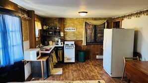 A compact kitchen with a stove, sink, and refrigerator, wooden flooring, and a 'Welcome' sign above the window.