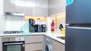 A compact kitchen with a gas stove, oven, microwave, coffee maker, and a washing machine. - Bloomfields 1BR Azizi Gardens Meydan (Dubai)