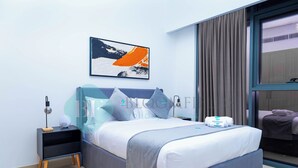 A modern bedroom with a bed, a bedside table, a nightstand, a window with curtains, and a wall-mounted abstract painting. - Bloomfields 1BR Azizi Gardens Meydan (Dubai)