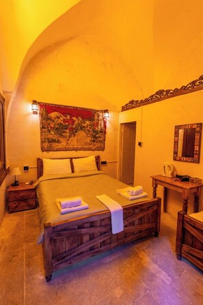 A bedroom with a large bed, a wooden headboard, a tapestry, a nightstand, a bedside table, and a mirror. - BEİRUT TAŞ KONAK OTEL (Sanliurfa)