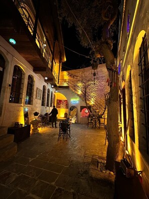 An outdoor courtyard with stone flooring, tables, chairs, and a staircase leading to an upper level. - BEİRUT TAŞ KONAK OTEL (Sanliurfa)