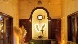 A cozy lounge area with a green sofa set, a tufted ottoman, and a decorative wall with a circular window. - BEİRUT TAŞ KONAK OTEL (Sanliurfa)